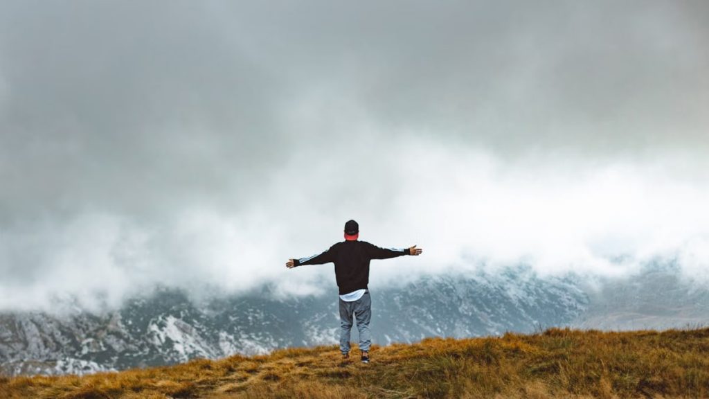 A lone traveler stands with arms outstretched, embracing the misty mountain view.